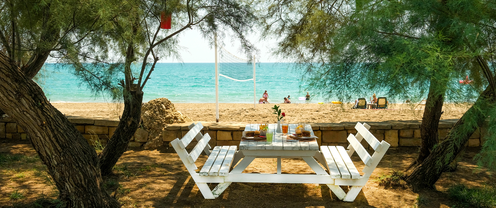 Gedeckter Tisch mit Bank und Stühlen im Schatten mit Blick aufs Meer