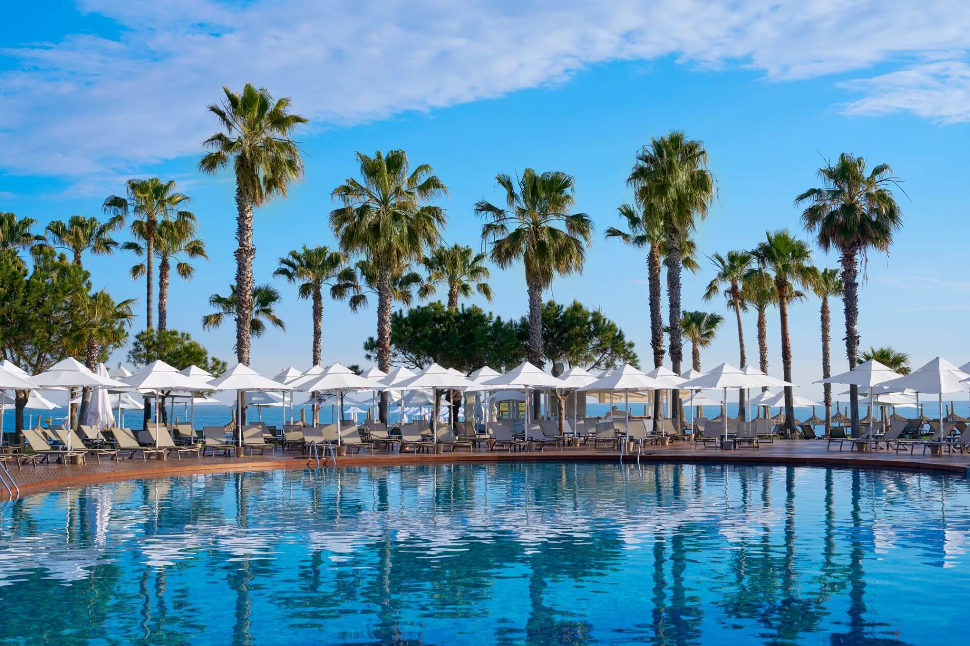 Hotelanlage mit Pool, Liegen, Sonnenschirmen und Palmen.