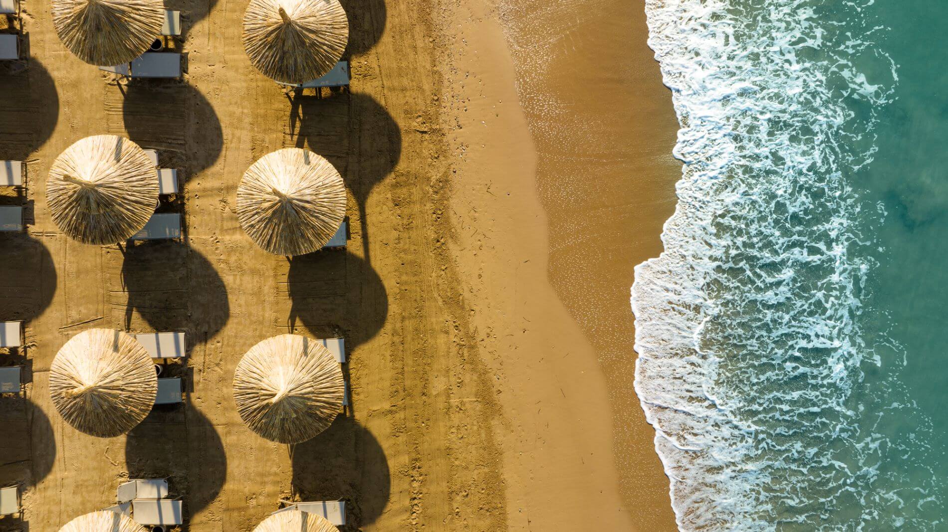 Strand in der Vogelperspektive mit Sonnenschirmen und -liegen.