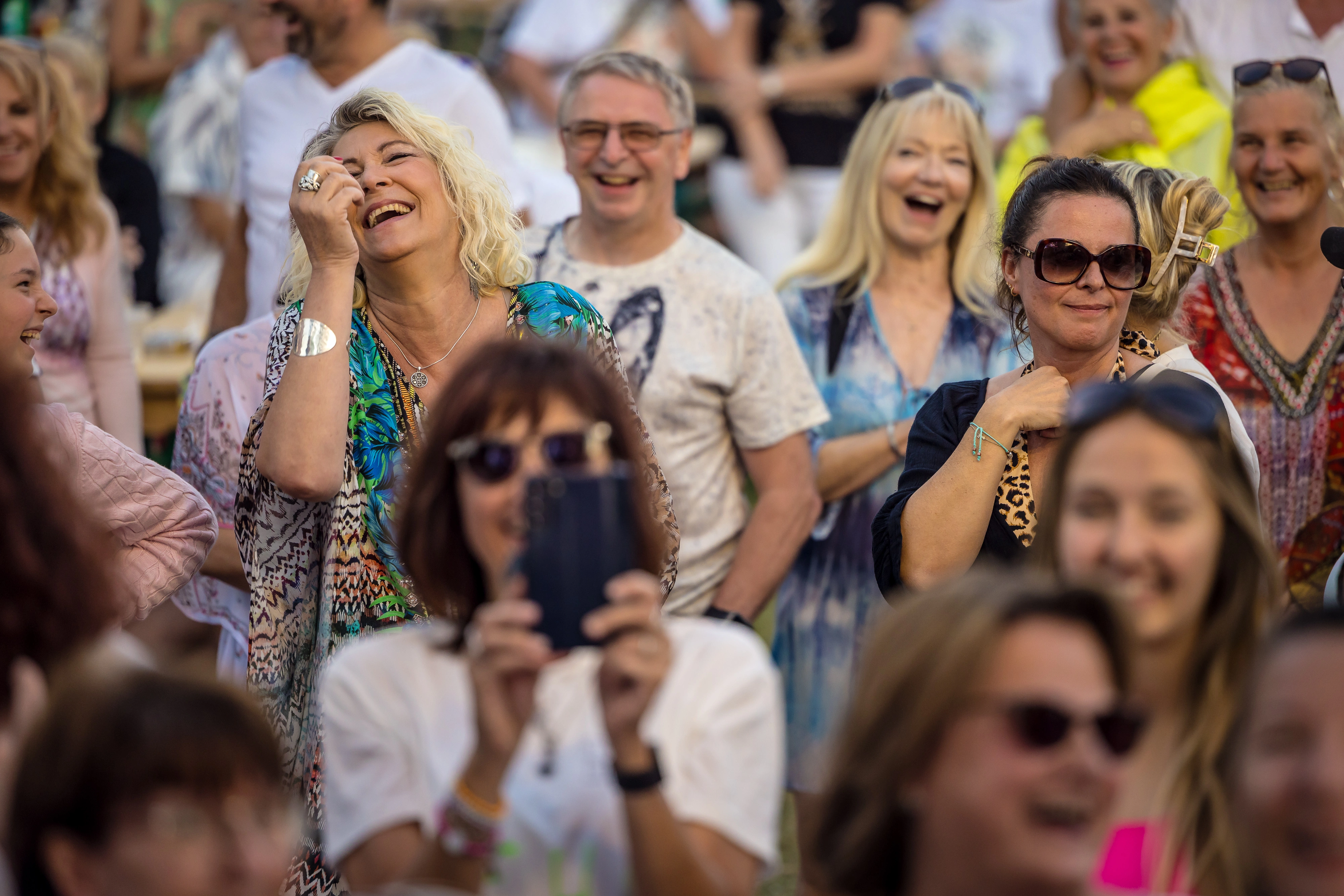 Freunde lachen zusammen an einem Tisch, halten Getränke in der Hand und genießen die Party. Fröhliche Gäste lachen und feiern gemeinsam bei einer Schlagerparty.