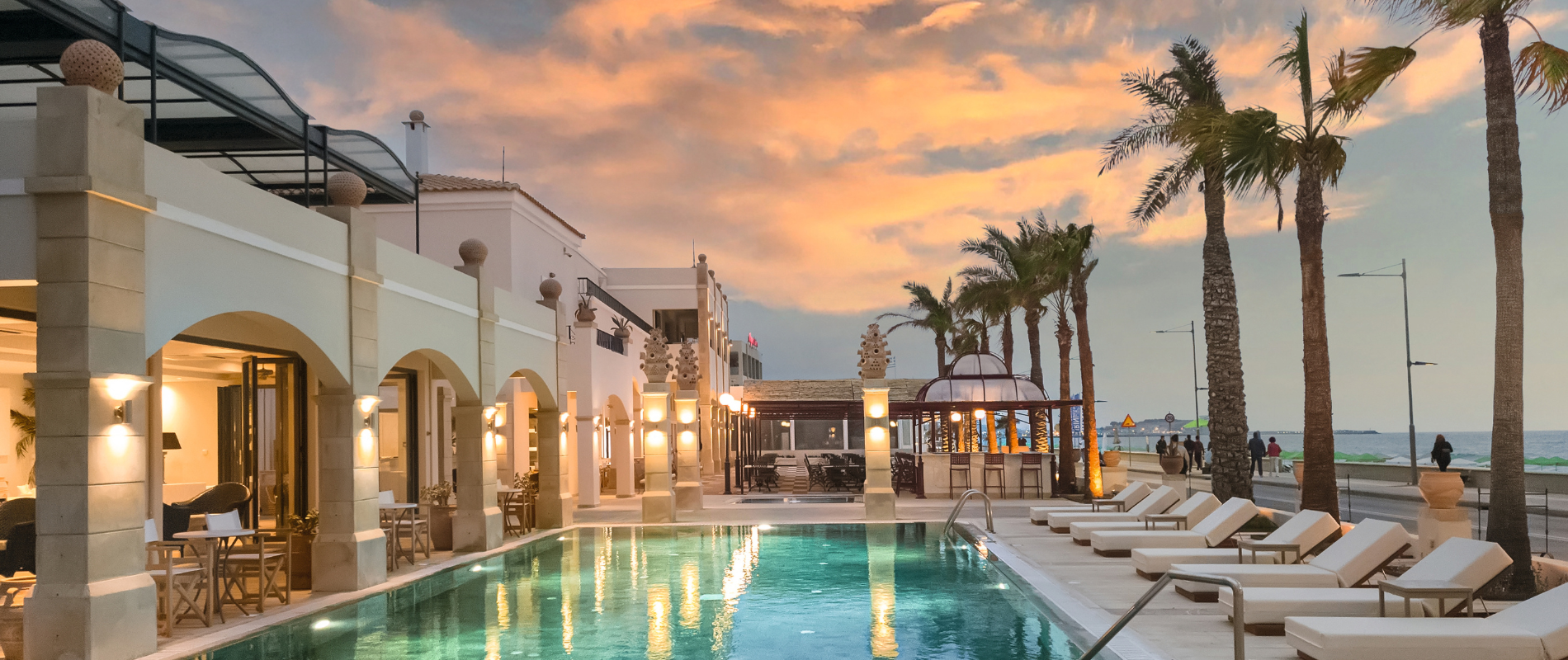 Poolanlage Hotelanlage mit Pool, Liegen, Sonnenschirmen und Palmen.