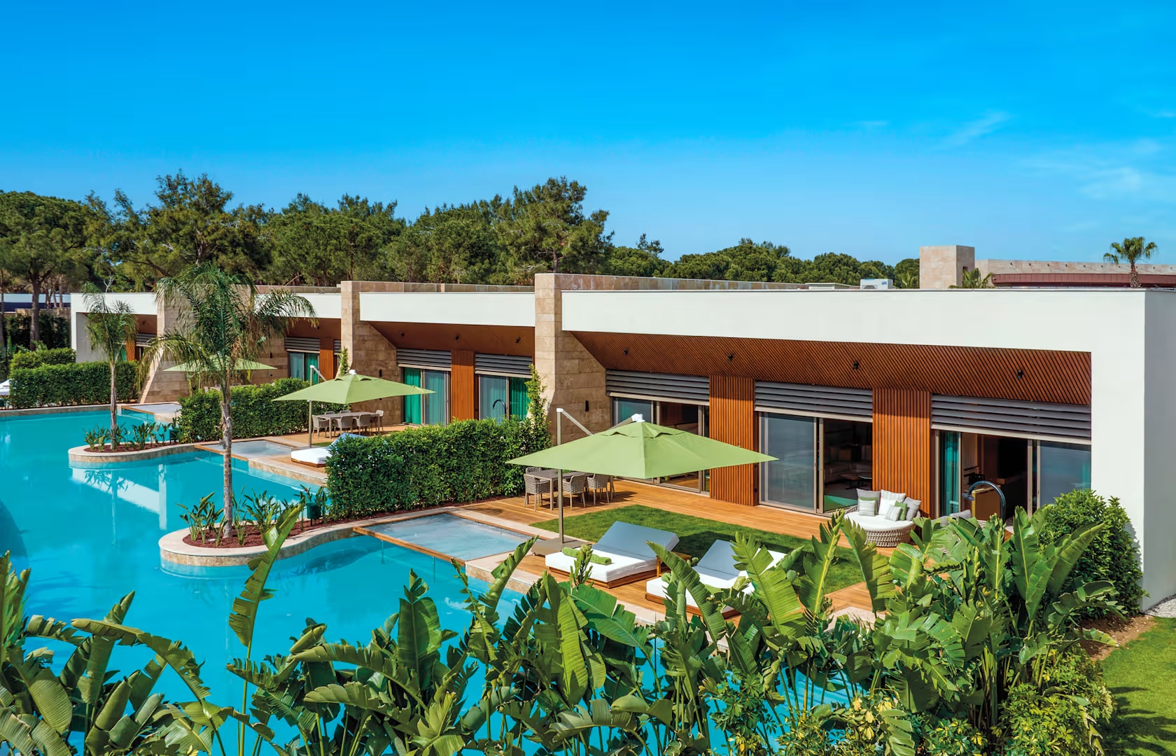 Hotelanlage Hotelanlage mit beigefarbenen Appartements, die eine minimalistische, quadratische Architektur aufweisen. Sie liegen direkt am Pool mit Palmen.